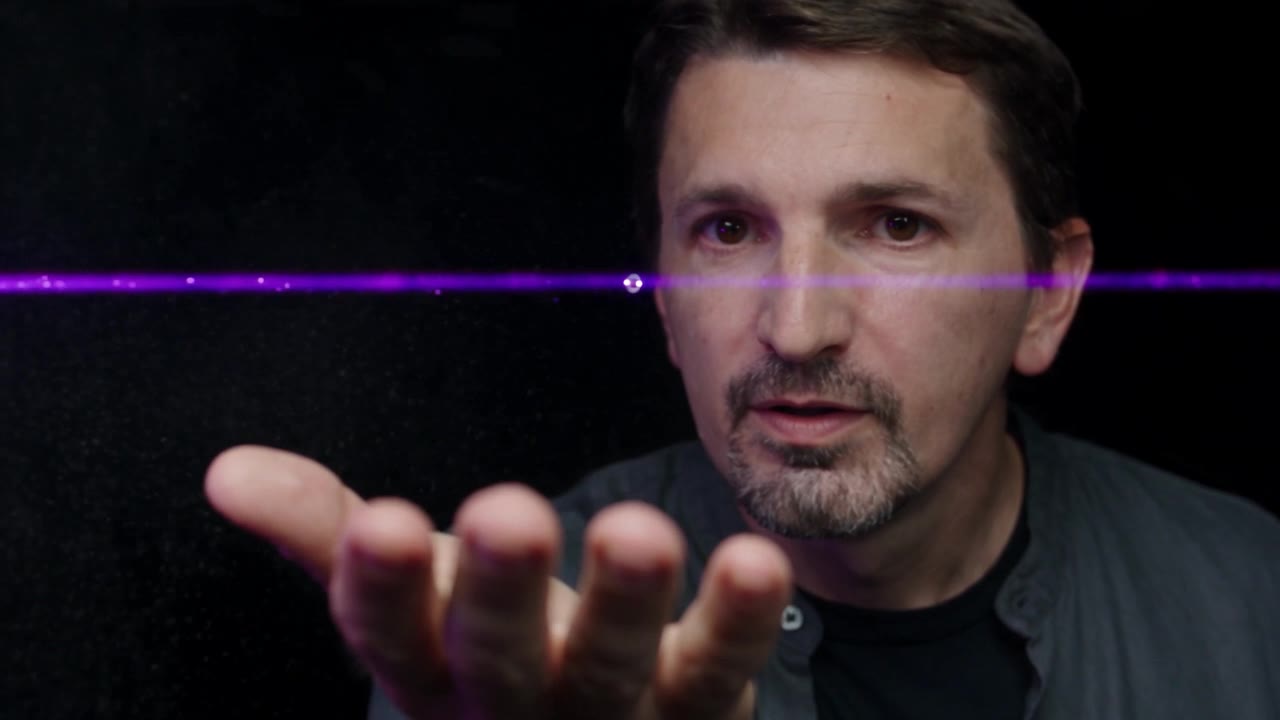 A hand held under a thin violet laser beam; the beam is only visible where dust crosses it.